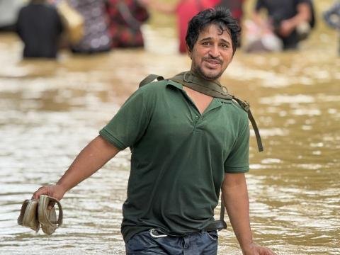 A man carries his shoes while walking through deep floodwater.
