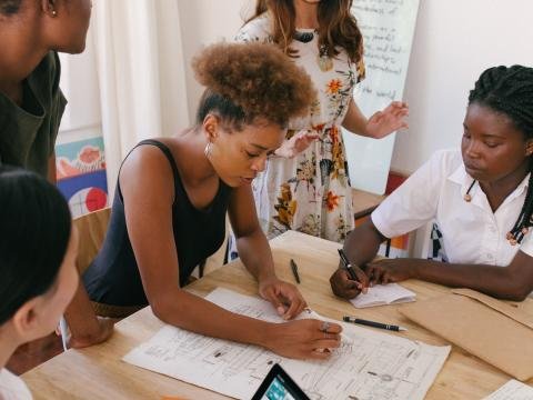 A diverse group of women collaborate around a table during a community workshop.