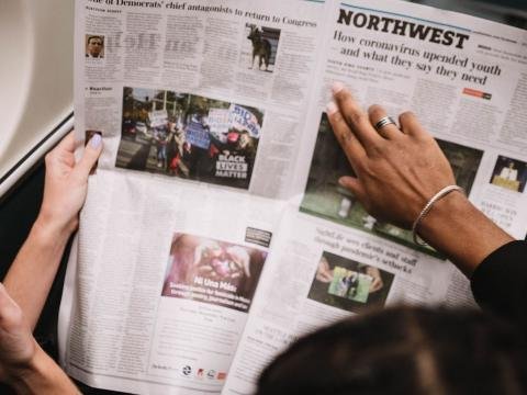 Two commuters read a newspaper together while travelling on a train.