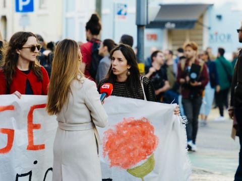 A journalist interviews women holding a handmade protest banner in a busy public space.