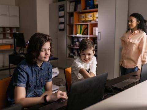 Students working on laptops while a teacher observes their classroom activity