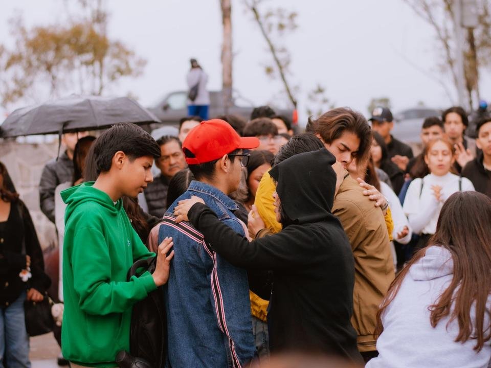 People comfort one another during a crowded outdoor gathering.